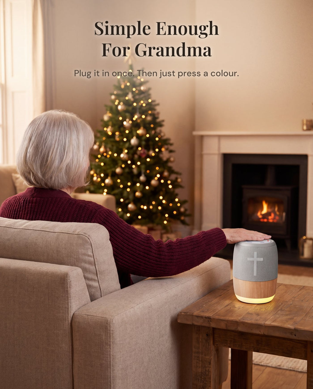A grandmother in her armchair, seen from behind, resting her hand on the player on the side table, a lit tree and fireplace beyond.